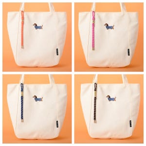 May include: Four off-white tote bags with different colored rope handles. Each bag features an embroidered dachshund wearing a blue polka-dot outfit. The rope handles are in shades of pink, orange, blue, and brown.