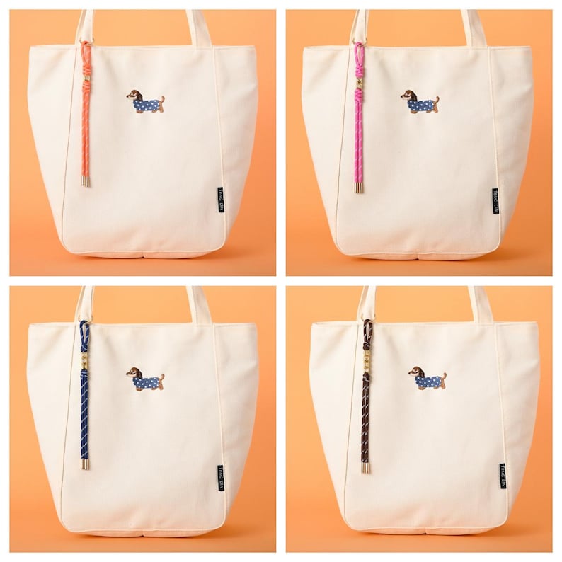 May include: Four off-white tote bags with different colored rope handles. Each bag features an embroidered dachshund wearing a blue polka-dot outfit. The rope handles are in shades of pink, orange, blue, and brown.