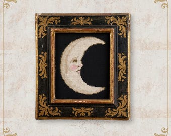May include: A framed cross-stitch of a crescent moon with a smiling face, set against a black background. The frame is black with gold accents and ornate detailing. The text "NobleLadyPupsik" is at the bottom.