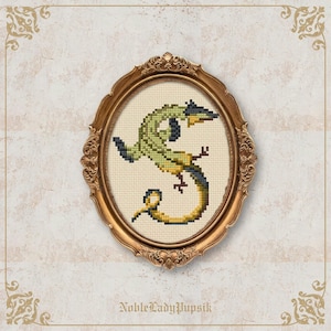 May include: Cross-stitch artwork of a green and yellow lizard in the shape of the letter "S" inside an oval gold frame. The frame is set against a textured, off-white background. The text "NobleLadyPupsik" is at the bottom.