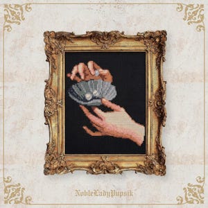 May include: Cross-stitch artwork in a gold ornate frame. The artwork depicts hands holding a shell with pearls. The hands are rendered in shades of pink and beige against a black background. The frame has intricate details and is set against a textured background. The text "NobleLadyPupsik" is at the bottom.