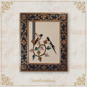 May include: Cross-stitch artwork of two birds perched on a vine with leaves and flowers, framed in a dark blue and gold ornate frame. The artwork is on a cream-colored background. The frame has floral and vine details.