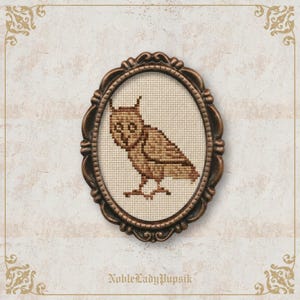 May include: A framed cross-stitch owl in shades of brown. The owl is centered within an oval frame with a decorative, dark brown border. The background is a cream-colored fabric. The text "NobleLadyPupsik" is at the bottom.