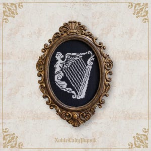 May include: An oval, ornate, gold-coloured frame surrounds a black background with a white cross-stitch design of a harp and a figure. The frame has decorative scrollwork. The text "NobleLadyPupsik" is at the bottom.