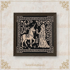 May include: A square cross-stitch embroidery in a dark brown frame featuring a black background with a cream-colored design of a unicorn and a person standing in a forest setting. The text NobleLadyPupsik is printed in small letters at the bottom.