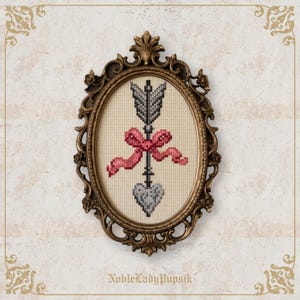 May include: Oval framed cross-stitch art featuring a gray arrow piercing a gray heart, adorned with a pink bow. The artwork is set against a cream-colored background and framed in an ornate gold-toned frame. The text "NobleLadyPupsik" is at the bottom.