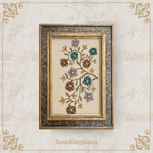 May include: A framed cross-stitch floral design. The artwork features a beige background with a branching pattern of colorful flowers in shades of blue, red, and purple. The frame is gold with dark blue accents.