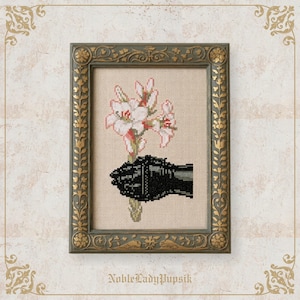 May include: Cross-stitch art of a black gloved hand holding white and pink flowers in a decorative frame. The frame is a muted green with gold accents. The background is a neutral beige.