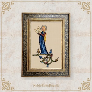 May include: A cross-stitch embroidery featuring a figure with long blonde hair wearing a blue gown and white head covering, holding an open book. The figure stands above a decorative vine motif with blue and brown leaves in a gold ornate frame.
