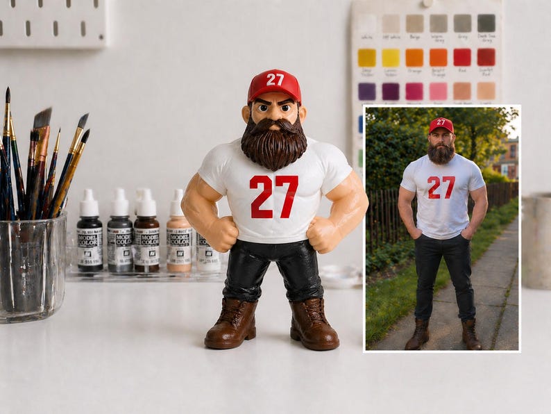 May include: A figurine of a muscular man with a beard, wearing a red cap, white t-shirt with the number 27, black pants, and brown boots. A smaller image of a man in similar attire is to the right.