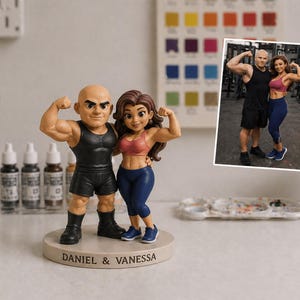 May include: A figurine of a muscular couple flexing their biceps. The male figure wears a black vest and shorts, while the female figure wears a pink sports bra and blue leggings. The base reads "DANIEL & VANESSA". A photo of the couple is in the background.