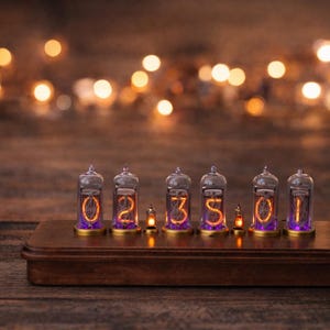 May include: A retro digital clock featuring six glass tubes showing the time. The numbers glow orange, set on a dark wooden base. A small succulent plant in a concrete pot is to the left.