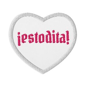 Könnte beinhalten: Ein weißes herzförmiges Patch mit einem grauen, denimartigen Rand. Das Patch zeigt das gestickte Wort "jestodita!" in einem leuchtenden Pink. Das Design ist einfach und auffällig.
