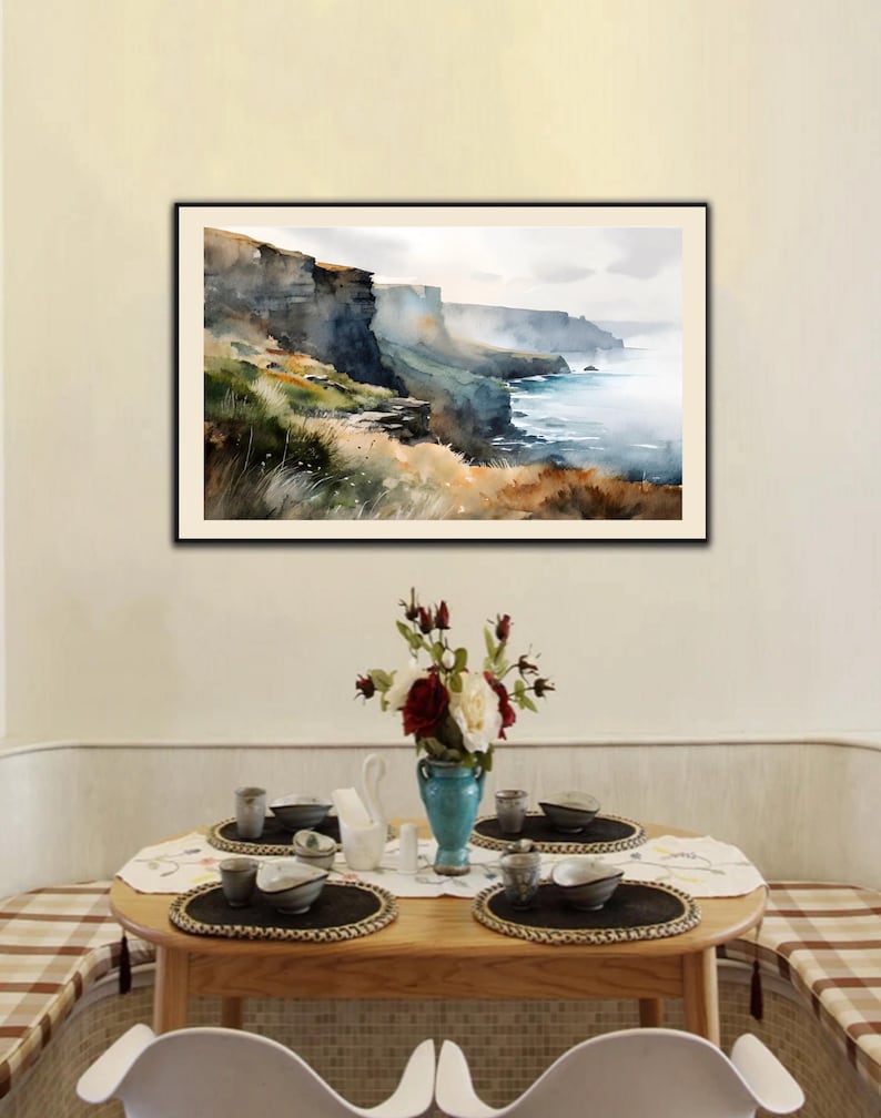 Puede incluir: Una pintura de acuarela enmarcada representa un paisaje costero con acantilados, oc&eacute;ano y un cielo brumoso. Debajo, una mesa de madera est&aacute; puesta con cubiertos, un jarr&oacute;n de flores y manteles individuales, creando una escena de comedor.