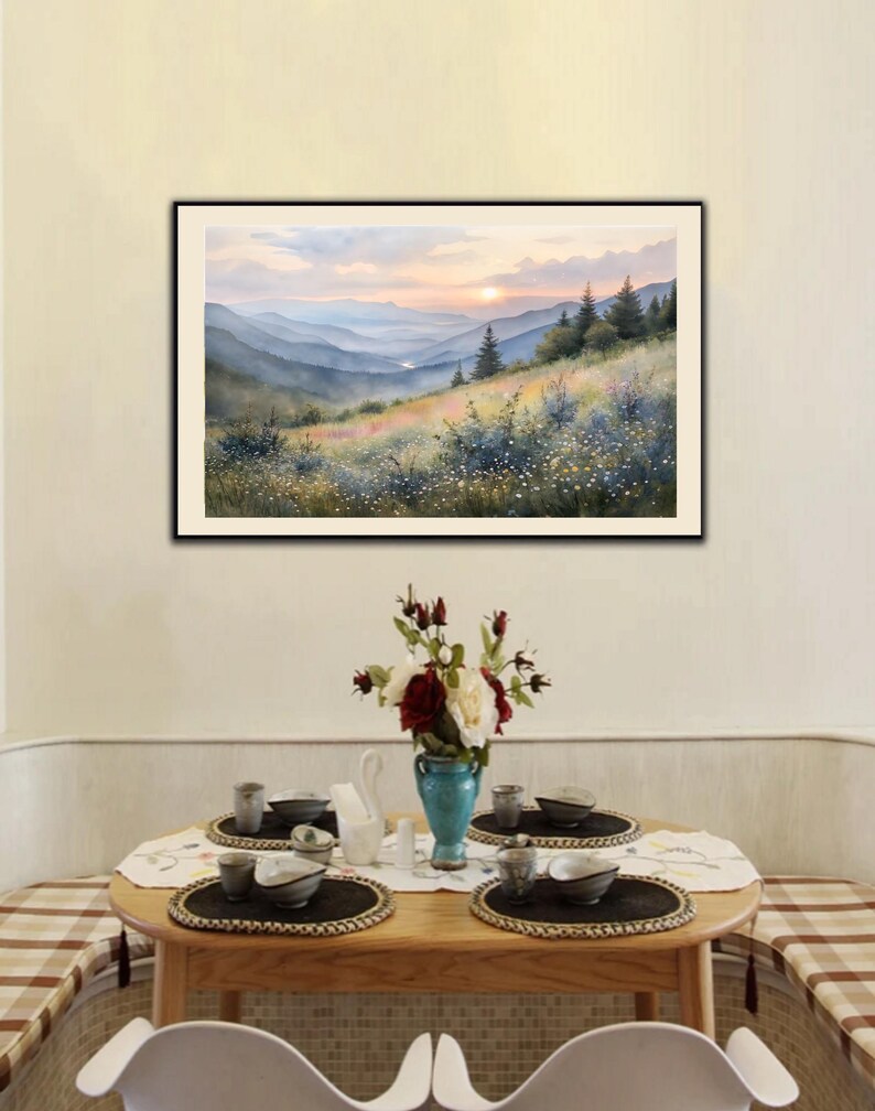 May include: A framed watercolor painting depicts a mountain landscape at sunset. The artwork features layers of blue mountains, a colorful meadow, and a vibrant sky. A dining table with place settings and a floral arrangement is in the foreground.