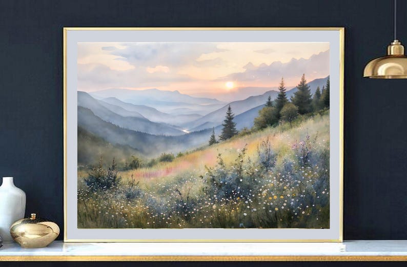 May include: A framed watercolor painting of a mountain landscape at sunset. The artwork features layers of blue-toned mountains, a grassy hillside with wildflowers, and a warm, golden sky. The frame is gold.