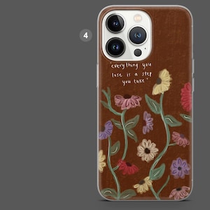 Puede incluir: Funda de tel&eacute;fono marr&oacute;n con dise&ntilde;o floral. La funda presenta la cita: "todo lo que pierdes es un paso que das". El dise&ntilde;o floral incluye flores en tonos rosa, amarillo y morado.