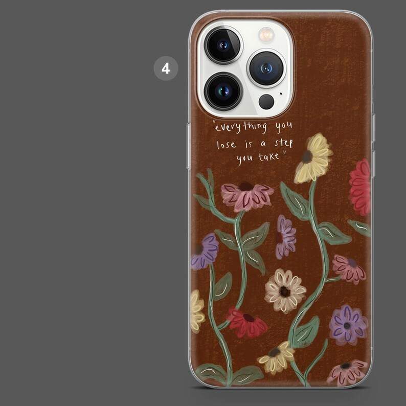 Puede incluir: Funda de tel&eacute;fono marr&oacute;n con dise&ntilde;o floral. La funda presenta la cita: "todo lo que pierdes es un paso que das". El dise&ntilde;o floral incluye flores en tonos rosa, amarillo y morado.