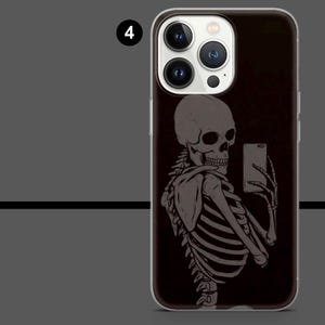 May include: A black phone case featuring a gray skeleton taking a selfie with a smartphone. The skeleton is depicted in a detailed, artistic style, with visible ribs and skull. The case has a clear border and a dark background.