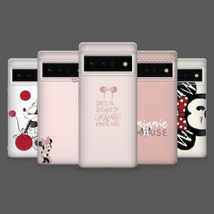 Puede incluir: Cinco fundas para teléfono en rosa y blanco con diseños variados. Presentan a Minnie Mouse y textos como "She's a Disney + Jesus kinda girl" y "Minnie Mouse". Dispuestas en fila sobre un fondo gris.