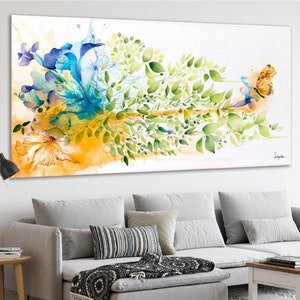 Abstract watercolor painting featuring a vibrant mix of blue, green, and yellow hues. The artwork depicts a stylized floral arrangement with a butterfly in flight. The painting is framed and displayed on a wall above a gray sofa.