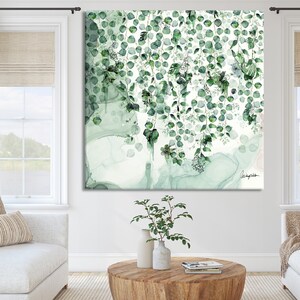 A square canvas print with a watercolor style design of green leaves and branches on a white background. The leaves are arranged in a cascading pattern, creating a sense of movement and depth. The artwork is signed in the bottom right corner with the artist's name.