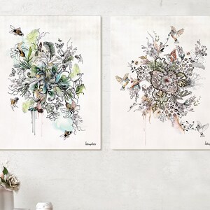 Two framed watercolor paintings with a floral theme. The paintings feature intricate details of flowers, leaves, and birds. The paintings are displayed on a light wood shelf with a light gray drawer.