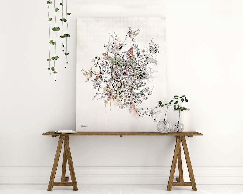 A black and white ink drawing of a floral design with birds and butterflies. The drawing is on a white canvas and is framed. The canvas is sitting on a wooden table with two small plants in glass vases.
