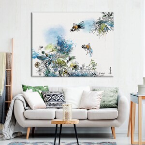 A watercolor painting of a white background with blue and green floral designs and two orange and black fish swimming. The painting is framed and hanging on a white wall above a white couch.