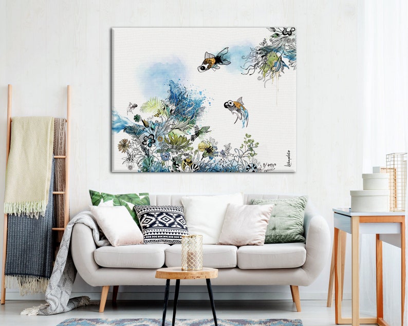 A watercolor painting of a white background with blue and green floral designs and two orange and black fish swimming. The painting is framed and hanging on a white wall above a white couch.