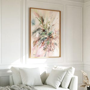 An abstract floral painting in a wooden frame. The artwork features a blend of soft pinks, greens, and beige hues, with brushstrokes creating a sense of movement and texture. The painting is displayed above a white sofa.