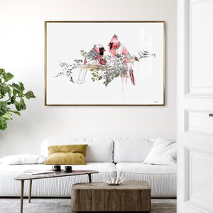 A rectangular wall art print featuring a watercolor illustration of two red cardinal birds perched on a branch surrounded by detailed botanical sketches in black ink, all set against a clean white background within a thin gold frame.