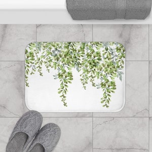 May include: White bath mat with a green leafy design. The leaves are arranged in a cascading pattern, creating a sense of movement and nature.