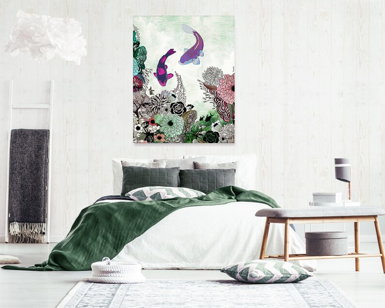 A green, white, and pink floral print with two purple and pink fish swimming in the water. The print is framed and hanging on a white wall above a white bed with green bedding. The bed has two pillows, one green and one white with a black and white geometric pattern. A wooden bench with a gray cushion is in the foreground.