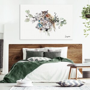 A watercolor painting of an owl perched on a branch with green leaves and flowers. The painting is framed and hanging on a white wall above a bed with green and white bedding.