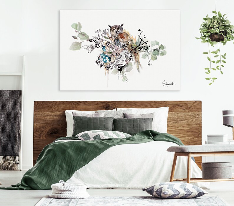 A watercolor painting of an owl perched on a branch with green leaves and flowers. The painting is framed and hanging on a white wall above a bed with green and white bedding.