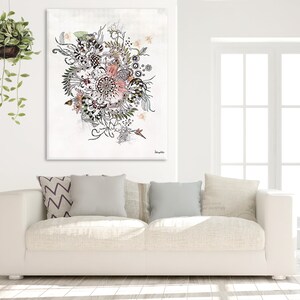 A white couch with three pillows, one with a chevron pattern and two with a solid color. A black and white floral print canvas hangs above the couch. The canvas has a pink flower in the center and is surrounded by leaves and other floral elements. The canvas is signed 'Daphne's' in the bottom right corner.