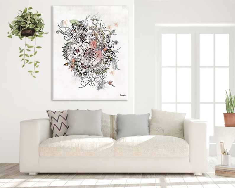 A white couch with three pillows, one with a chevron pattern and two with a solid color. A black and white floral print canvas hangs above the couch. The canvas has a pink flower in the center and is surrounded by leaves and other floral elements. The canvas is signed 'Daphne's' in the bottom right corner.