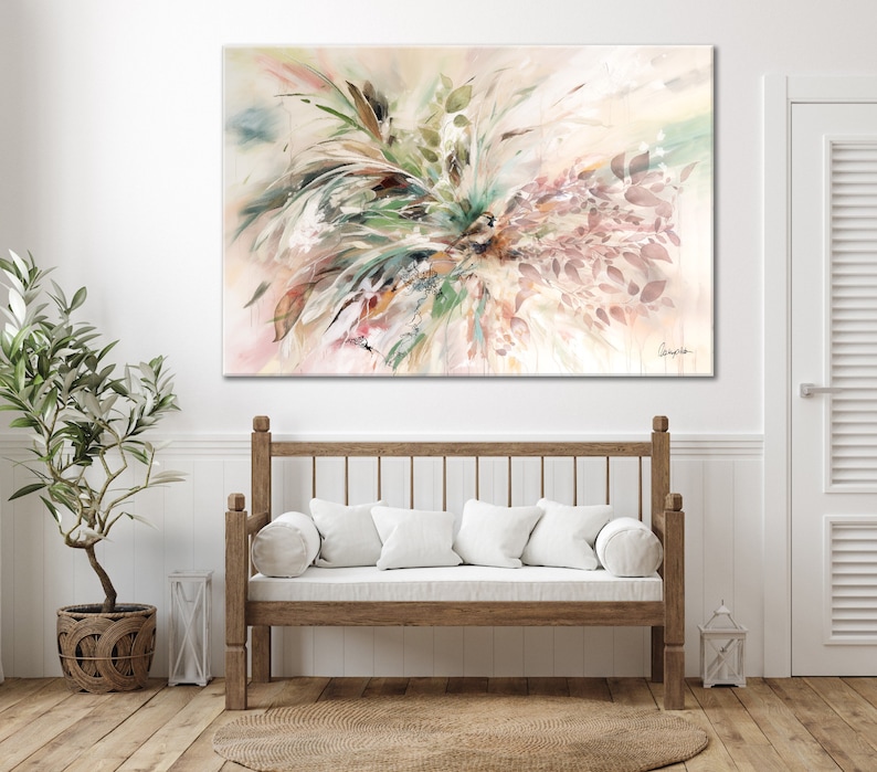 A large abstract watercolor painting with a white background and shades of pink, green, and brown. The painting features a cluster of leaves and branches in the center, with a few leaves extending out to the edges of the canvas. The painting is signed in the bottom right corner with the name 'Gingko'. The painting is hanging on a white wall above a wooden bench with white cushions.