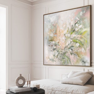 A large abstract painting with a light pink, green, and white color scheme. The painting depicts a cluster of flowers and leaves in a loose, impressionistic style. The painting is framed in a thin, gold-colored frame and is hanging on a white wall.