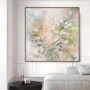A large abstract painting with a light pink, green, and white color scheme. The painting features a floral design with soft brushstrokes and a textured surface. The painting is framed in a light wood frame and is hanging on a white wall.