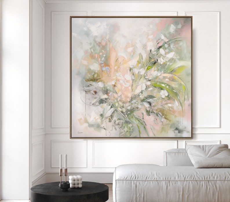 A large abstract painting with a light pink, green, and white color scheme. The painting features a floral design with soft brushstrokes and a textured surface. The painting is framed in a light wood frame and is hanging on a white wall.