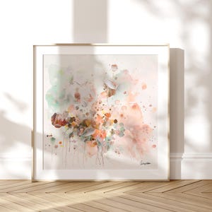 Square framed art print featuring an abstract floral watercolor painting. The artwork showcases a blend of soft colors, including peach, pink, green, and brown, with delicate brushstrokes and splatters. The painting is signed in the bottom right corner.