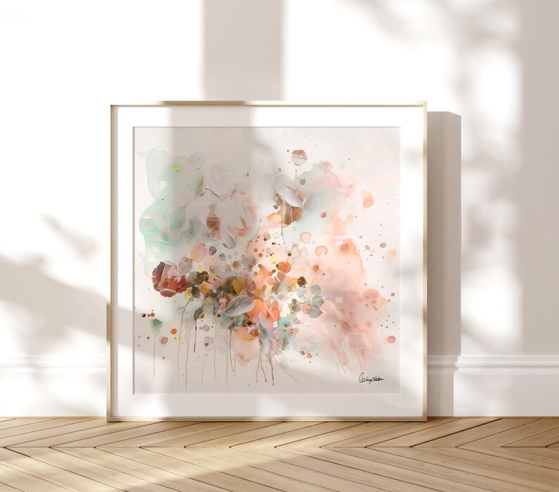 Square framed art print featuring an abstract floral watercolor painting. The artwork showcases a blend of soft colors, including peach, pink, green, and brown, with delicate brushstrokes and splatters. The painting is signed in the bottom right corner.