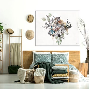 A bedroom with a wooden bed, a green patterned duvet, and a large canvas print of an owl with green leaves and branches. The canvas print is hanging on a white wall. There are two wicker baskets on the floor, a wooden ladder with a beige blanket hanging on it, and a green plant in a brown pot on the right side of the image.