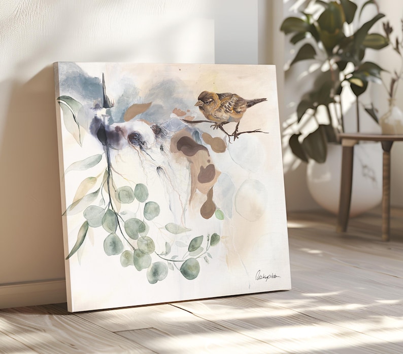 A square watercolor painting features a small brown bird perched on a branch of eucalyptus leaves. The background is a soft blend of beige, light blue, and brown watercolor washes.  The painting has a delicate, nature-inspired theme. The artist's signature is subtly placed in the bottom right corner.