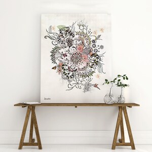 A black and white floral illustration with pink and green accents on a canvas print. The print is hanging on a white wall above a wooden table with two glass vases containing green plants.