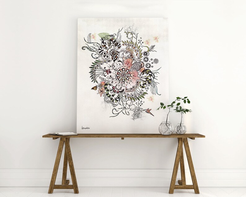 A black and white floral illustration with pink and green accents on a canvas print. The print is hanging on a white wall above a wooden table with two glass vases containing green plants.