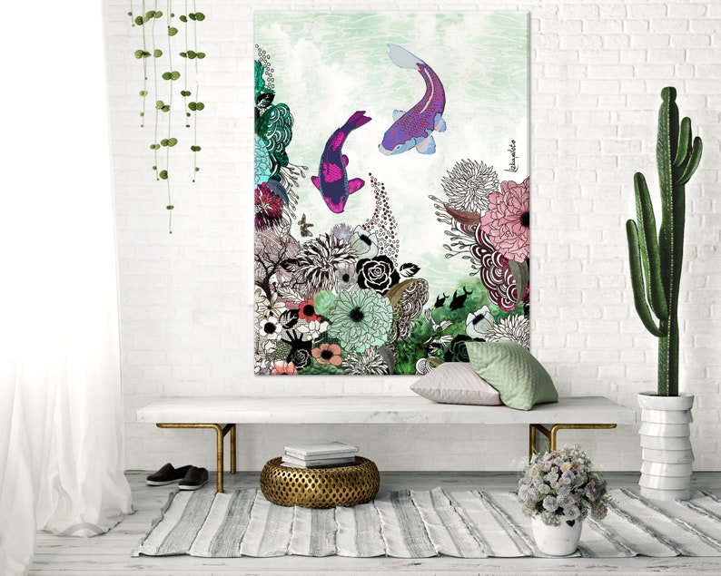 A white canvas print with a green, pink, and purple floral design. Two purple and pink fish are swimming in the water. The print is hanging on a white brick wall above a white bench. There are two green plants on the floor, one in a white pot and the other in a brown pot.