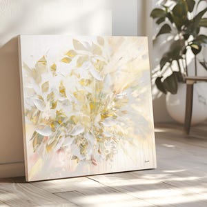 Square canvas art featuring a floral abstract design in white, cream, and gold. The artwork has a textured appearance with visible brushstrokes, creating a sense of depth and movement. The painting is leaning against a wall.